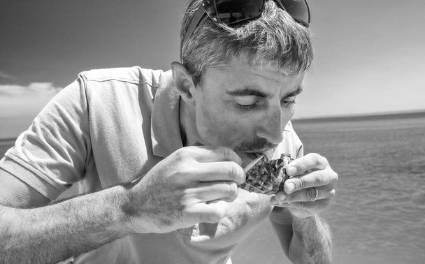 Homem comendo uma ostra fresca ao ar livre ao longo do oceano - Foto, Imagem