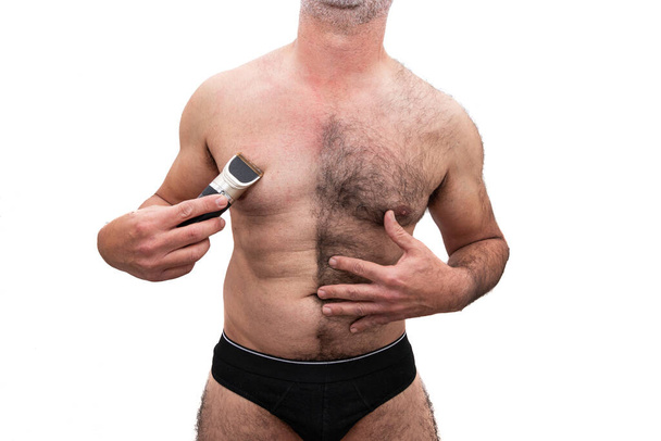 Egy atlétikai idősebb fehér férfi, csupasz mellű szőrös, borotvát tart a kezében, félig borotvált mellkassal. Fehér alapon elszigetelve. - Fotó, kép