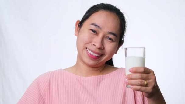 Boldog nő tejet iszik üvegből, és feladja a hüvelykujját a fehér háttér stúdióban. Egészséges táplálkozás. - Felvétel, videó