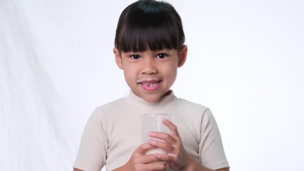 Asiatique petite fille mignonne boire du lait à partir d'un verre et sourire sur fond blanc en studio. Une alimentation saine pour les jeunes enfants. - Séquence, vidéo
