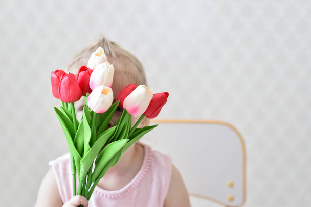 A bouquet of beautiful tulips in the hands of a child who is hiding behind a bouquet. The concept of Mother's Day, Women's Day. copy space - Foto, Bild