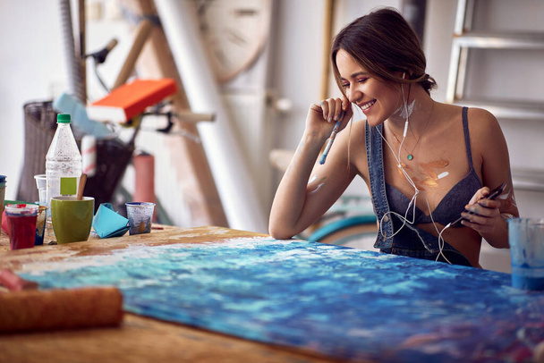 A young sexy and attractive female artist is having a good time while listening to the music and working on a new painting in a relaxed atmosphere in her studio. Art, painting, studio - 写真・画像