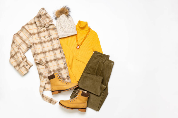 Female winter or autumn stylish clothing set. Plaid checkered shirt, yellow sweater and leather boots, green corduroy trousers, hat with pompom. Trendy fashionable casual clothes. Fashion concept. - Fotografie, Obrázek