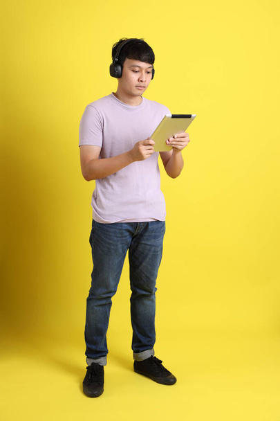 The young adult Asian man standing on the yellow background. - Foto, afbeelding