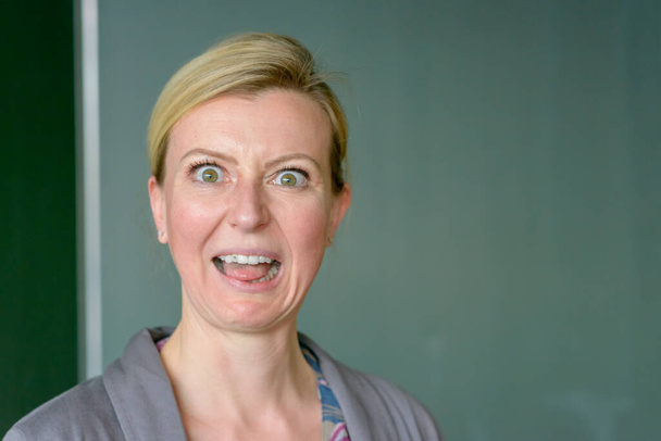 Teacher pulling an aghast face in front of blackboard staring at the camera with wide eyes and open mouth - Photo, Image