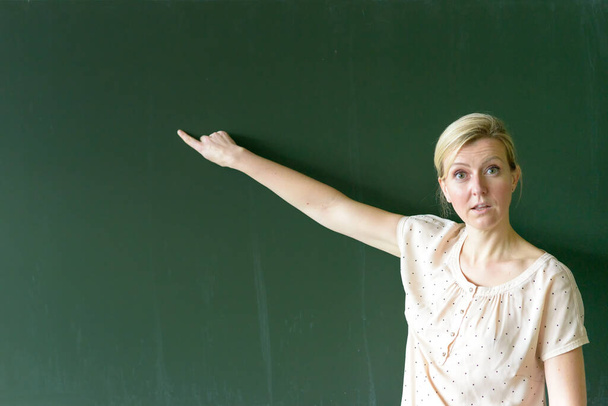 Учитель указывает на пустое место на доске с выражением ужаса, когда она преподает в классе - Фото, изображение