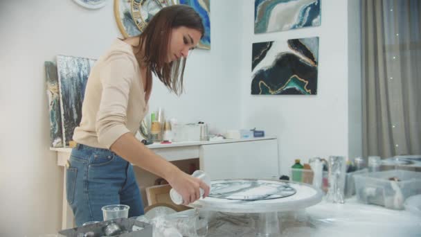 Mujer joven termina la pintura de resina epoxi en una forma de reloj y verter piezas claras alrededor de la circunferencia para la textura - Imágenes, Vídeo