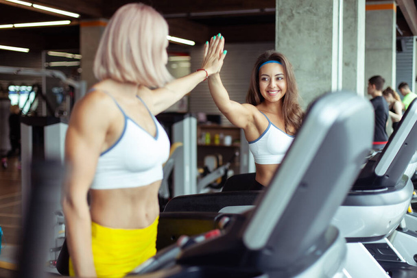 Zwei athletische Frauen befreunden sich mit High-Five, während sie auf einem Laufband trainieren. Gesunder Lebensstil - Foto, Bild
