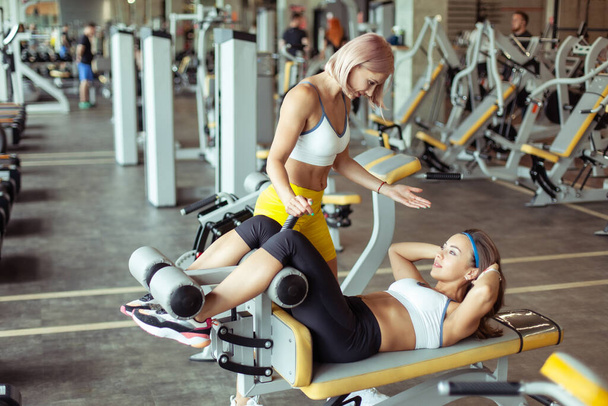 ジムで運動をする女性と彼女のトレーナーを適合させなさい。パーソナルトレーナー運動機械の女性訓練を調整します。 - 写真・画像