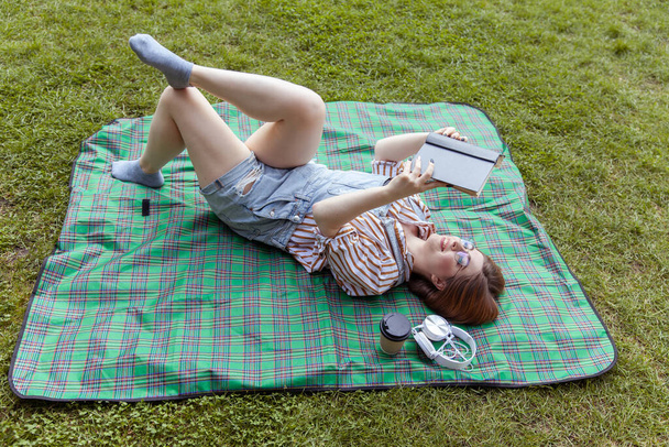 Junge Studentin liest Buch, während sie im Park auf einer Decke liegt - Foto, Bild