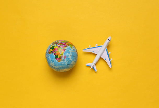Zabawkowy samolot pasażerski i kula ziemska na żółtym tle. Podróż, podróże, wakacyjna koncepcja. Widok z góry - Zdjęcie, obraz