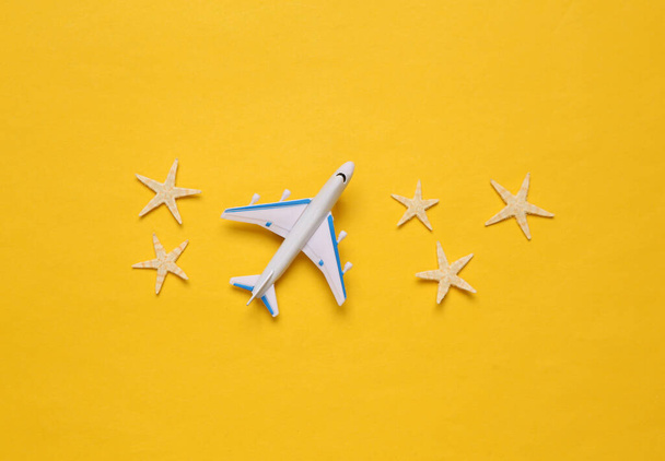 Juguete avión de pasajeros y estrellas de mar sobre fondo amarillo. Viaje, viaje, concepto de vacaciones de verano. Vista superior - Foto, imagen