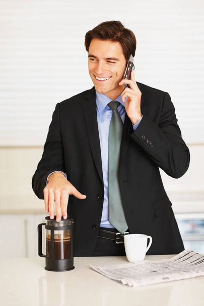 Executivo feliz usando celular enquanto bebe café em casa. Jovem executivo feliz usando celular enquanto bebe café no balcão da cozinha. - Foto, Imagem