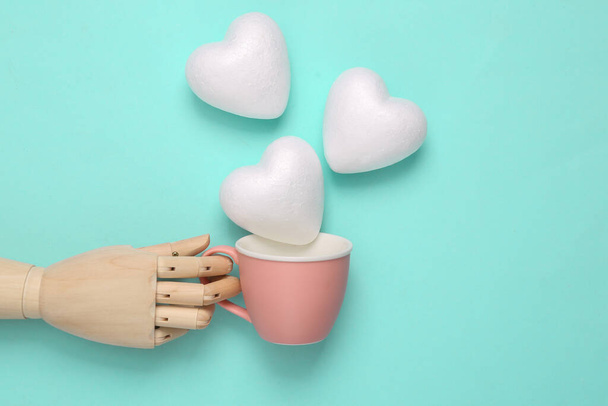 Wooden hand holding cup with hearts on blue pastel background. Romantic, love concept. Top view - Photo, Image
