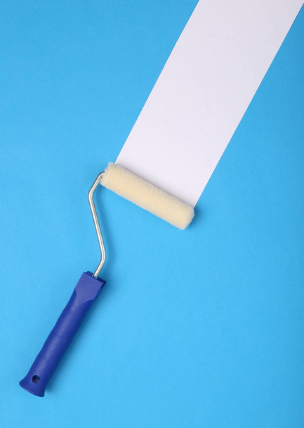 Rullo di vernice con striscia bianca su sfondo blu. Concetto di ristrutturazione casa  - Foto, immagini