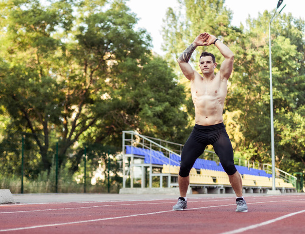 Athletischer Mann mit nacktem Oberkörper beim Aufwärmen, bevor er ins Stadion läuft. Gesunder Lebensstil - Foto, Bild