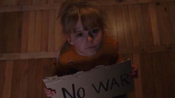 Paura ragazza senzatetto bambino seduto in possesso di iscrizione Nessuna guerra, nascondersi da bombardamento attacco a casa - Filmati, video