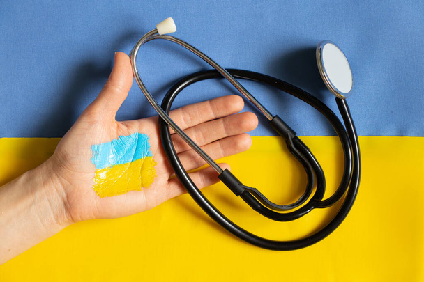 Stethoskop in der Hand liegt auf der ukrainischen Nationalflagge gelb-blau, Kriegsrecht in der Ukraine, medizinische Versorgung im Krieg - Foto, Bild