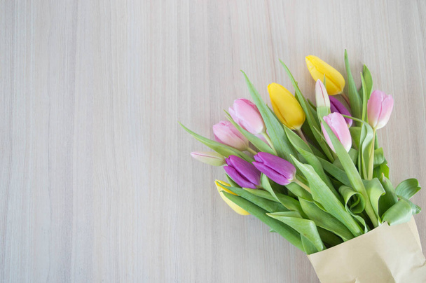 yellow, pink and purple tulips on light brown wooden ground with space for text background - Fotoğraf, Görsel