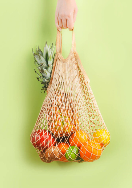 Woman hand holding eco friendly shopping bag with various tropical fruits on green background. Sustainable lifestyle. Plastic free. Zero waste concept - Zdjęcie, obraz