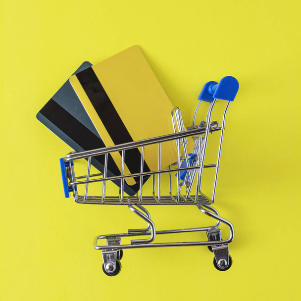 toy metal mini trolley with bank cards on a yellow background. Flat lay, mockup and copy space. - Фото, зображення