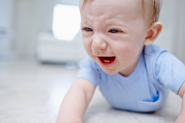 Teething is not fun. Closeup of a very unhappy baby boy lying on the floor. - Fotografie, Obrázek