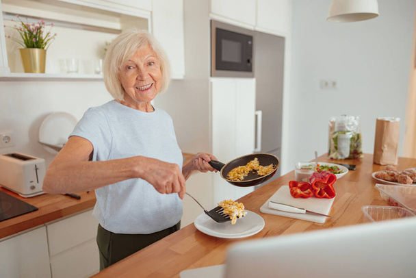 年配の女性が自宅のキッチンで料理をつくる - 写真・画像