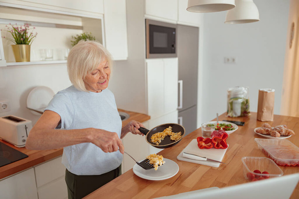 Pozitív nyugdíjas nő, aki ételt szolgál fel otthon - Fotó, kép
