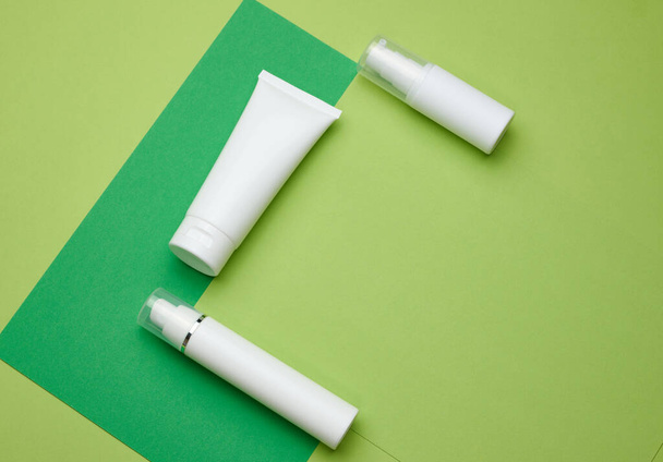 бутылки и пустые белые пластиковые трубки для косметики на зеленом фоне. Упаковка для крема, геля, сыворотки, рекламы и продвижения продукта - Фото, изображение