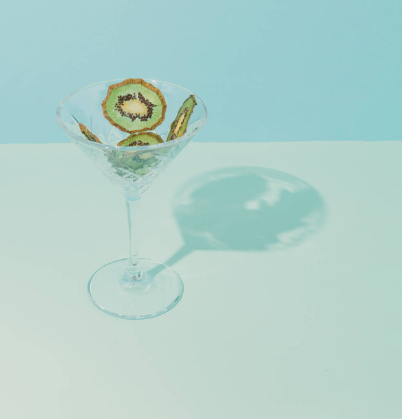 Modern conceptual setting of still life. Dried fruit in a cocktail glass. Blue background and green kiwi. - Photo, Image