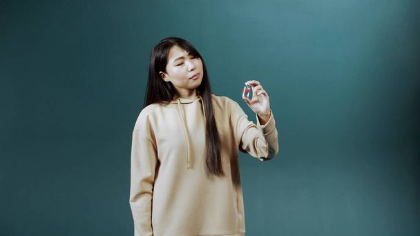 Uma jovem mulher asiática atraente não aconselha esta ampola com a vacina contra o coronavírus e mostra um polegar para baixo - Foto, Imagem