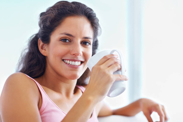Young woman having a cup of coffee. Closeup of a young woman smiling and looking at you while having a cup of coffee. - Foto, imagen