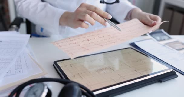 El cardiólogo examina el electrocardiograma del paciente en el primer plano del comprimido - Imágenes, Vídeo