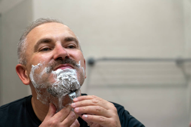 Orta yaşlı yakışıklı adam banyoda sakalını kesiyor. - Fotoğraf, Görsel