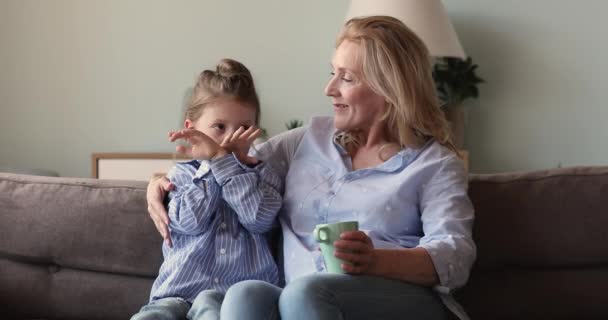 Older grandmother relaxing on sofa holds cup talks to granddaughter - Filmagem, Vídeo
