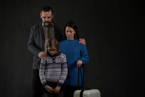 Refugee family with one child looking down on black background, Ukraine war concept. - Foto, immagini