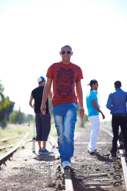 Mantendo o caminho certo. Tiro de um jovem caminhando pelas trilhas do trem enquanto seus amigos estão no fundo. - Foto, Imagem