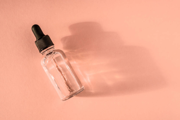 Transparent glass dropper bottle with air bubbles on beige background in the sunlight - Photo, Image