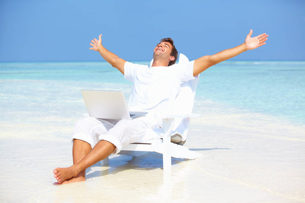 Pryč od hektického života. Portrét bezstarostného muže roztahujícího ruce s laptopem na pláži. - Fotografie, Obrázek