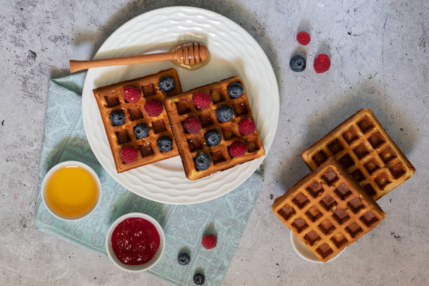 Traditional waffles with blueberries, raspberries and honey on light background - Photo, image