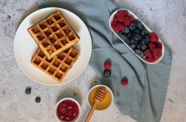 Homemade waffles with raspberries, blueberries and honey on light background - Photo, Image