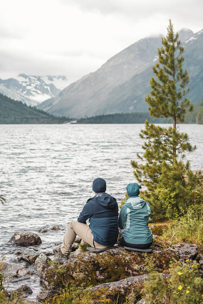 愛のカップルは、北部の山の中で素晴らしい絵のような湖の海岸に座っています。国立公園を巡る旅 - 写真・画像