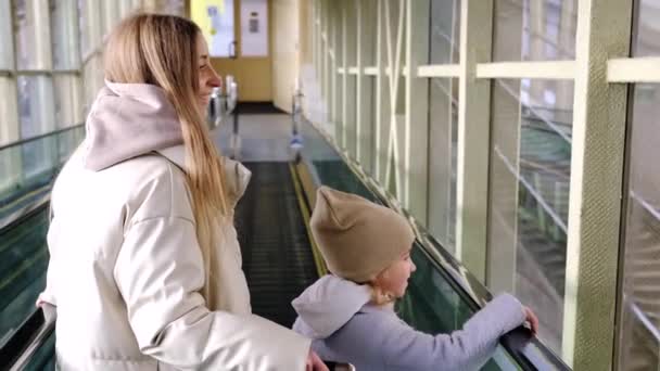 Mom and daughter go down the escalator from the station building to the platform - Footage, Video