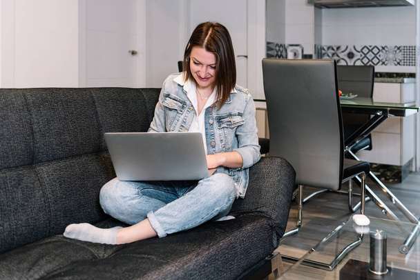 Mujer usando un ordenador portátil mientras está sentado en un sofá en la sala de estar en casa. - Foto, imagen