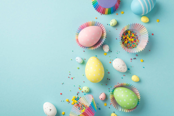 Top view photo of easter decor composition multicolored easter eggs in paper baking molds and confectionery topping on isolated pastel blue background with empty space - Foto, afbeelding