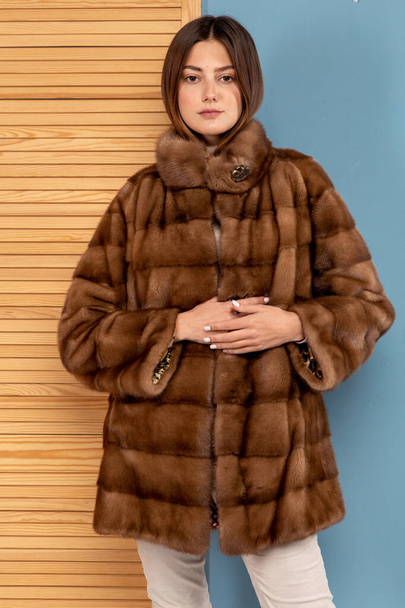 A beautiful girl with dark hair poses in a fur coat - Foto, Imagen
