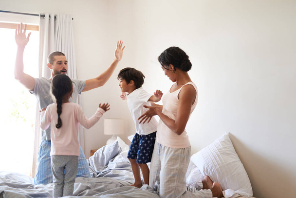 Het plezier stopt nooit in ons huis. Shot van een mooie jonge familie van vier plezier hebben en tijd samen doorbrengen in hun slaapkamer thuis. - Foto, afbeelding