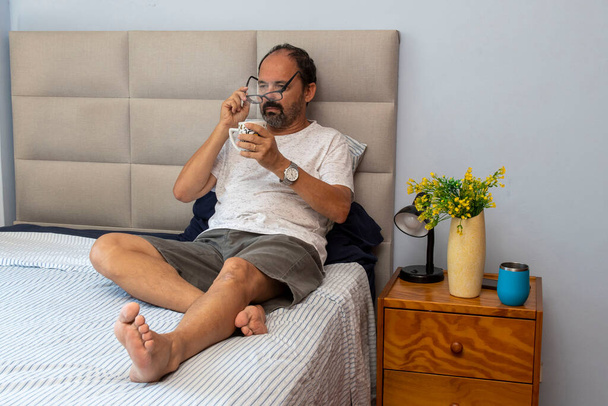 Hombre mayor sentado en la cama bebiendo café - Foto, Imagen