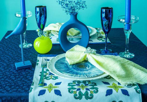 Table setting in blue and yellow colors. On a dark tablecloth a plate, a vase of flowers and decor - 写真・画像