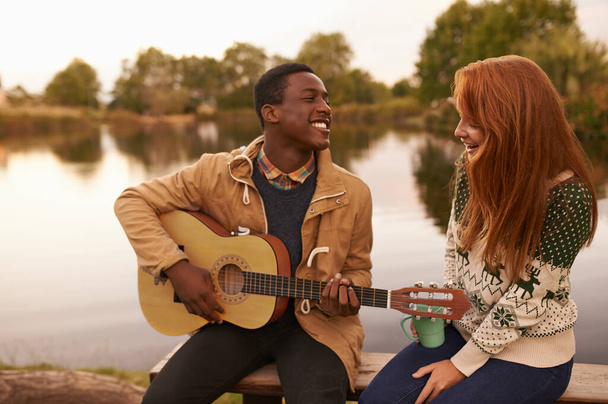 Mostrando le sue abilita '. Un bel giovane uomo serenata una bella ragazza mentre seduto accanto a un lago. - Foto, immagini